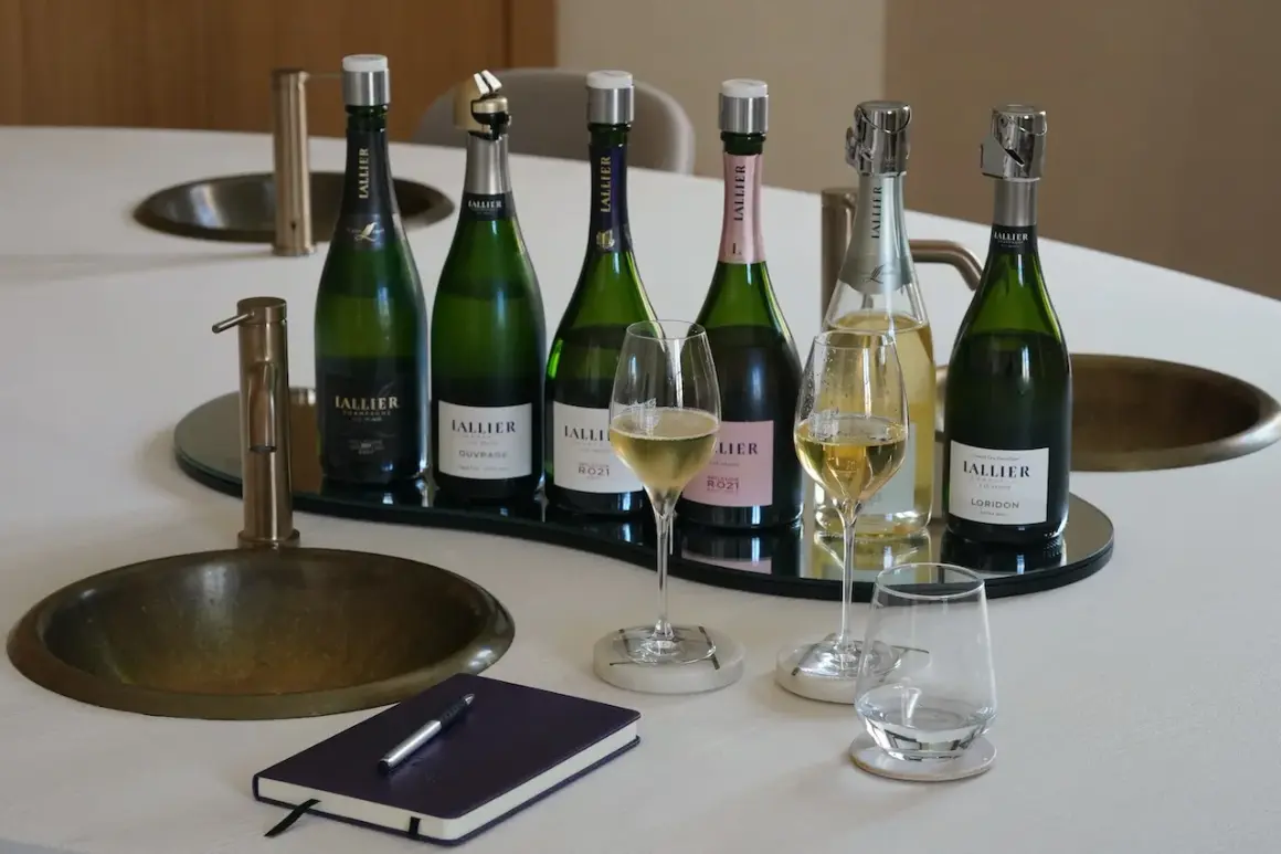 Sechs Flaschen LALLIER Champagner, vielleicht der beste Champagner der Welt, stehen bereit. Zwei Gläser sind gefüllt, bereit für eine Verkostung.
