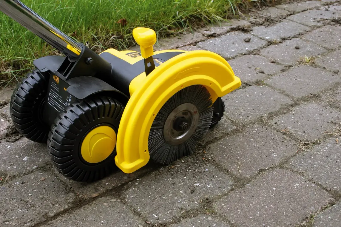 Żółta elektryczna zamiatarka do kostki z czarnymi kołami i szczotką, gotowa do pracy na podjeździe.