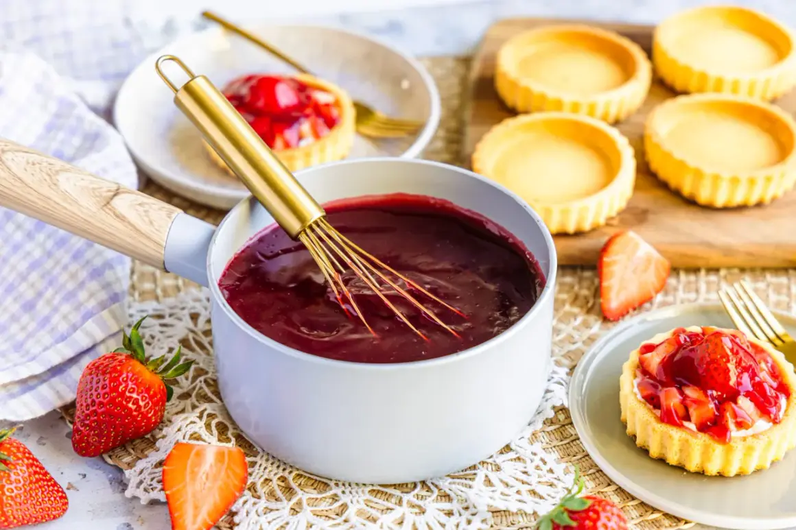 Frische Erdbeeren und ein Topf mit glänzendem Fruchtgelee – so gelingt tortenguss selber machen perfekt für leckere Törtchen.