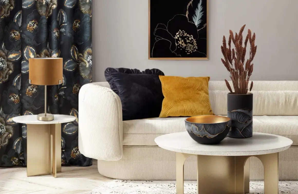 Elegancki salon z kanapą, ozdobnymi poduszkami i wazonem z suszonymi trawami zamiast kwiatów. Złote akcenty i ciemne zasłony tworzą przytulną atmosferę.