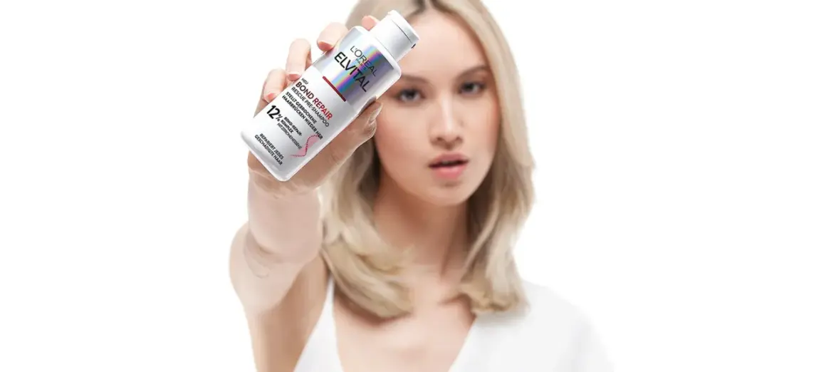 Frau zeigt L'Oréal Elvital Bond Repair Pre-Shampoo gegen extrem trockene Haare. Vorher-Nachher-Effekt für geschädigtes Haar.