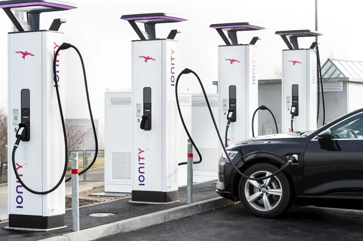 Une voiture électrique noire est branchée à une borne de recharge Ionity. Plusieurs bornes sont alignées, prêtes à alimenter les véhicules.