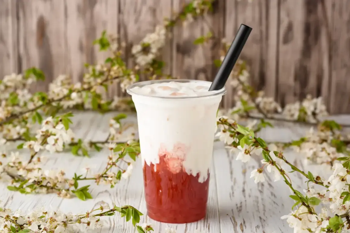 Jak zrobić bubble tea? Pyszny napój z truskawkowym syropem i mleczną pianką, ozdobiony kwitnącymi gałązkami.