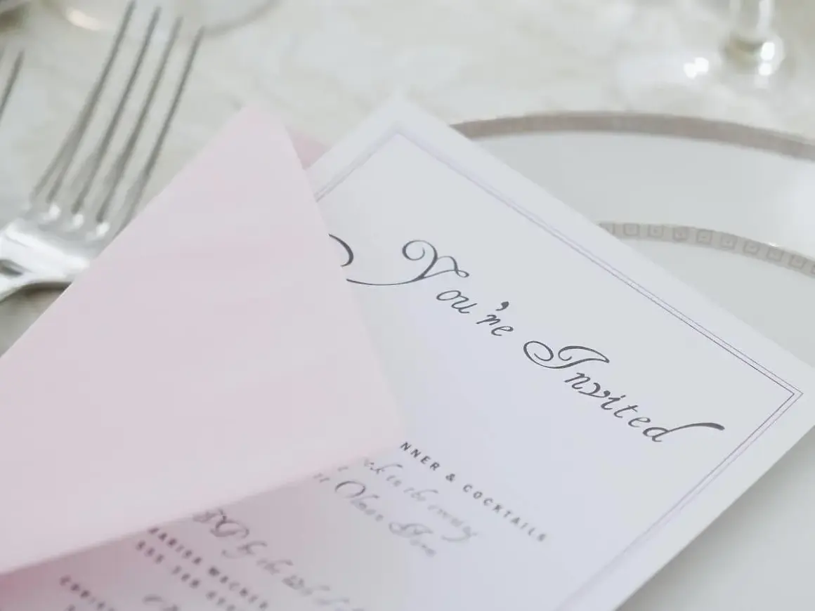 Eleganckie zaproszenie z napisem "You're Invited" i różową kopertą. Wskazówka, jak pisać na zaproszeniu z osobą towarzyszącą.