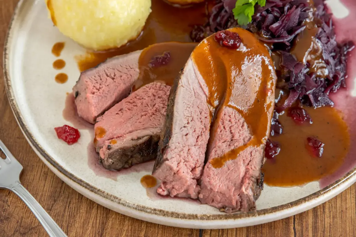 Saftiges Rehschulter Rezept: Rosa gebratenes Fleisch mit Sauce, Rotkohl und Klößen auf einem Teller.