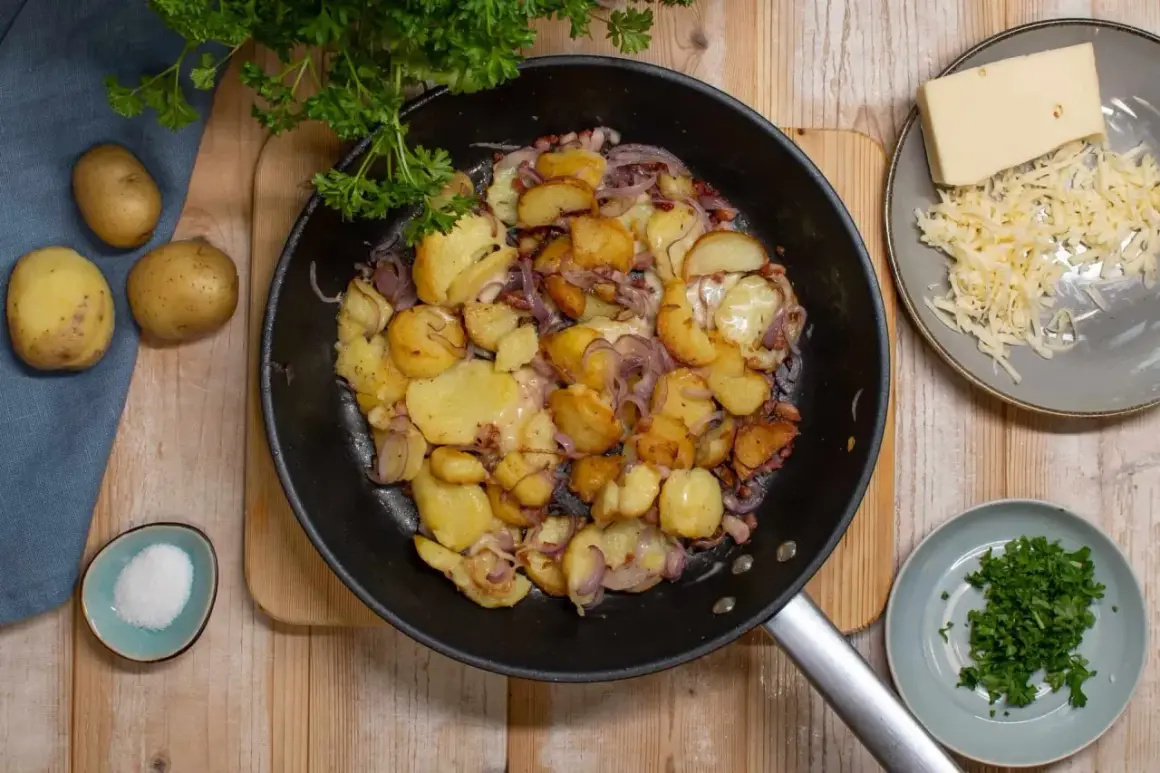 Bratkartoffeln aus rohen Kartoffeln, Zwiebeln und Speck in der Pfanne, dazu geriebener Käse und Petersilie.