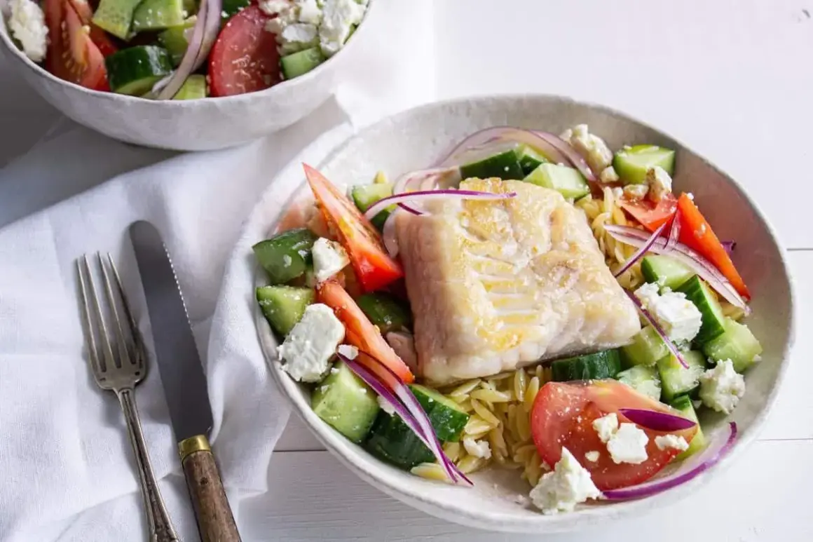 Salade de poisson méditerranéenne avec poisson blanc poêlé, concombre, tomate, oignon rouge et feta sur un lit de pâtes orzo.