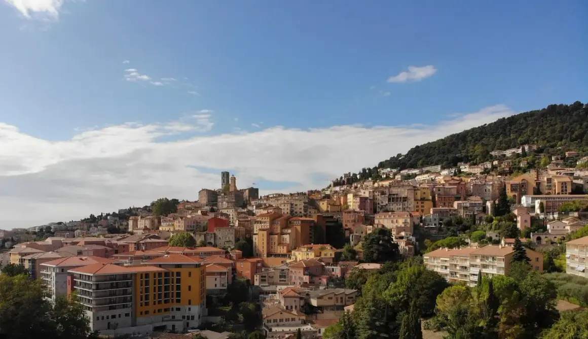 Widok na miasteczko na wzgórzu, z kolorowymi budynkami i zielenią, przypominający scenerię z festiwalu Cannes.