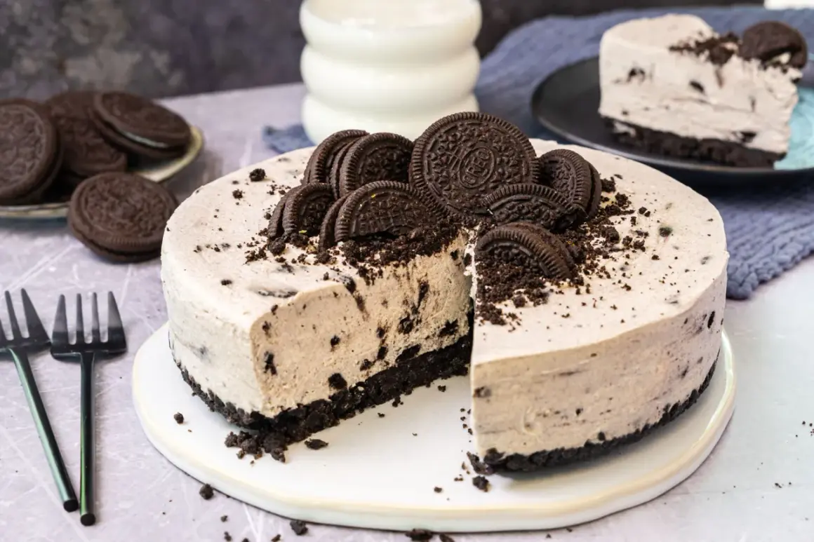 Cremige Oreo Torte mit Biskuitboden, dekoriert mit ganzen und halben Keksen. Ein Stück ist bereits angeschnitten.