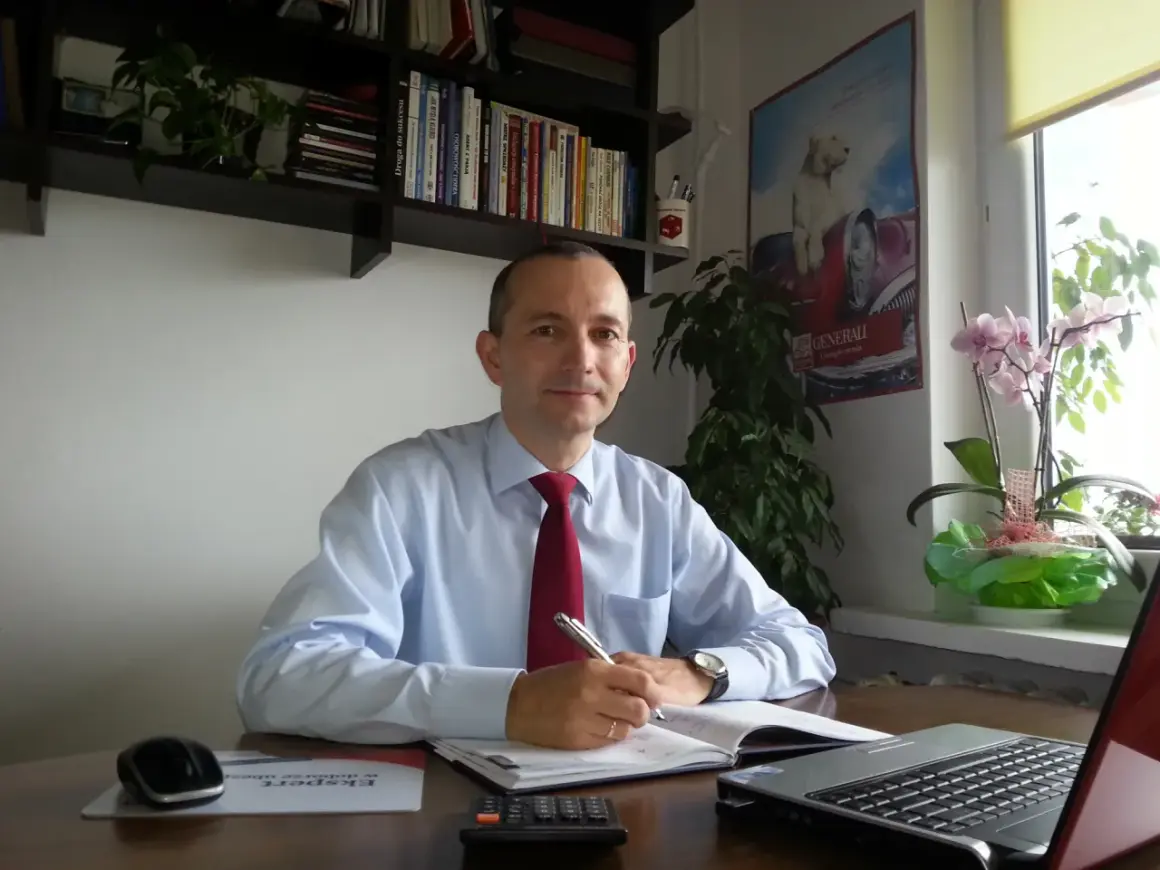 Mężczyzna w jasnej koszuli i czerwonym krawacie siedzi przy biurku, pisząc w notatniku.