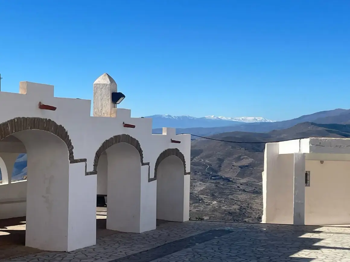Arcos blancos y un paisaje montañoso nevado en la sierra de Almería bajo un cielo azul.