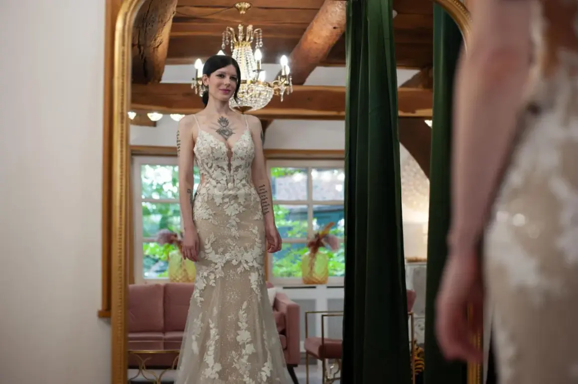 Braut steht vor Spiegel in einem figurbetonten Brautkleid mit Tüll und Spitze.