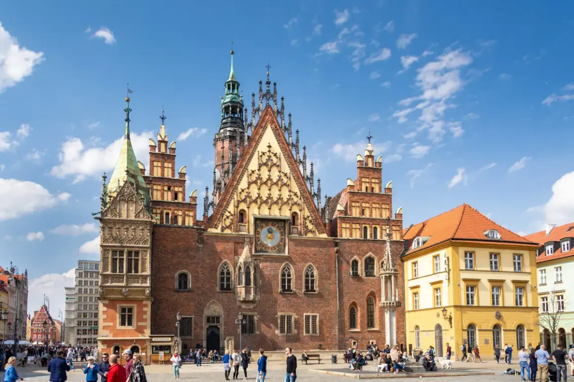 Stary Rynek we Wrocławiu tętni życiem. Wspaniały Ratusz z zegarem astronomicznym dominuje nad placem, gdzie spacerują ludzie.