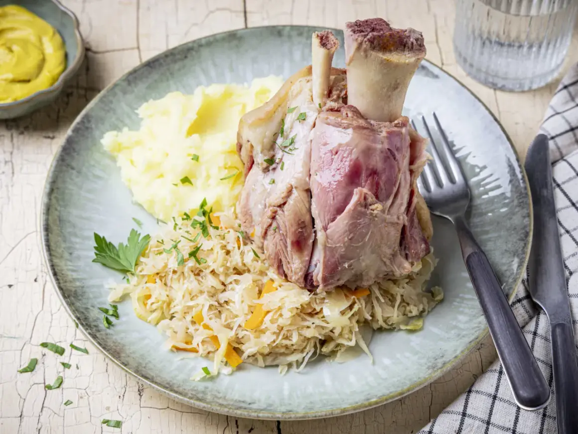 Deftig zubereitetes Eisbein in Sauerkraut kochen, serviert mit Kartoffelpüree und Senf.