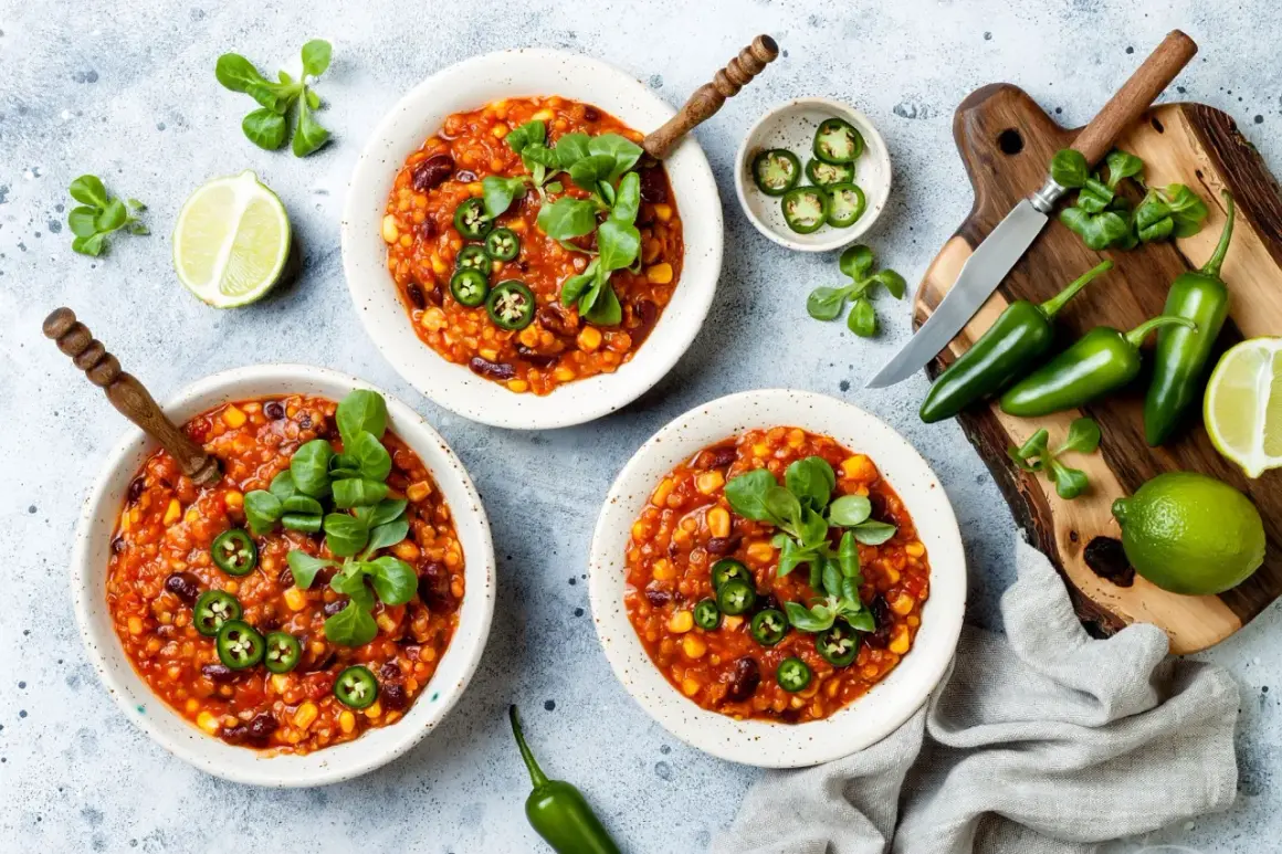 Pyszne chili con carne wege w miseczkach, ozdobione zielonymi listkami i plasterkami jalapeño. Obok limonki i papryczki.