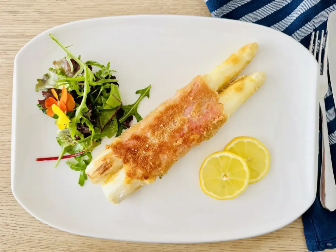 Spargel Cordon Bleu, knusprig paniert, serviert mit frischem Salat und Zitronenscheiben auf einem weißen Teller.
