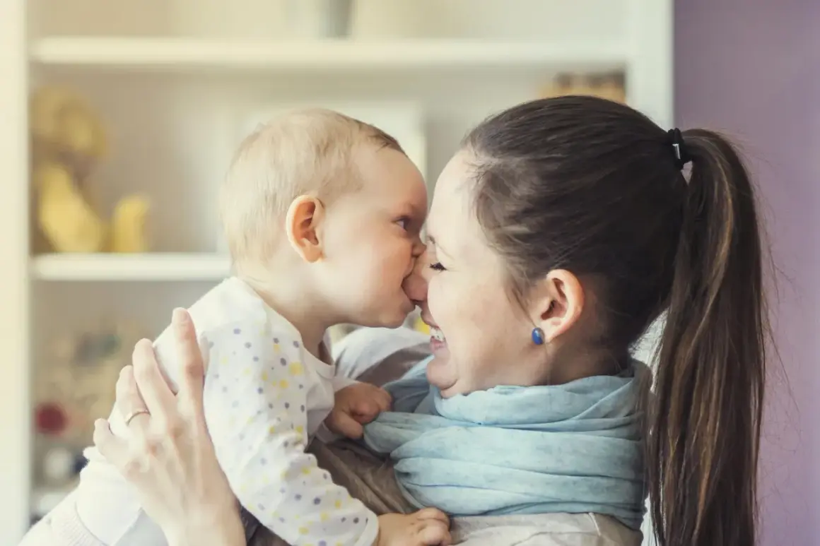 Ein süßer Moment zwischen Mutter und Baby (24 Wochen alt). Das Baby gibt der Mutter einen Nasenkuss, beide lächeln glücklich.