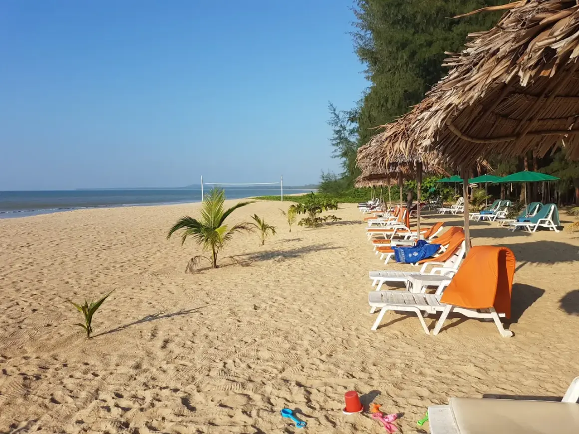 Solig strand på Koh Kho Khao med solstolar, parasoller och en volleybollplan.