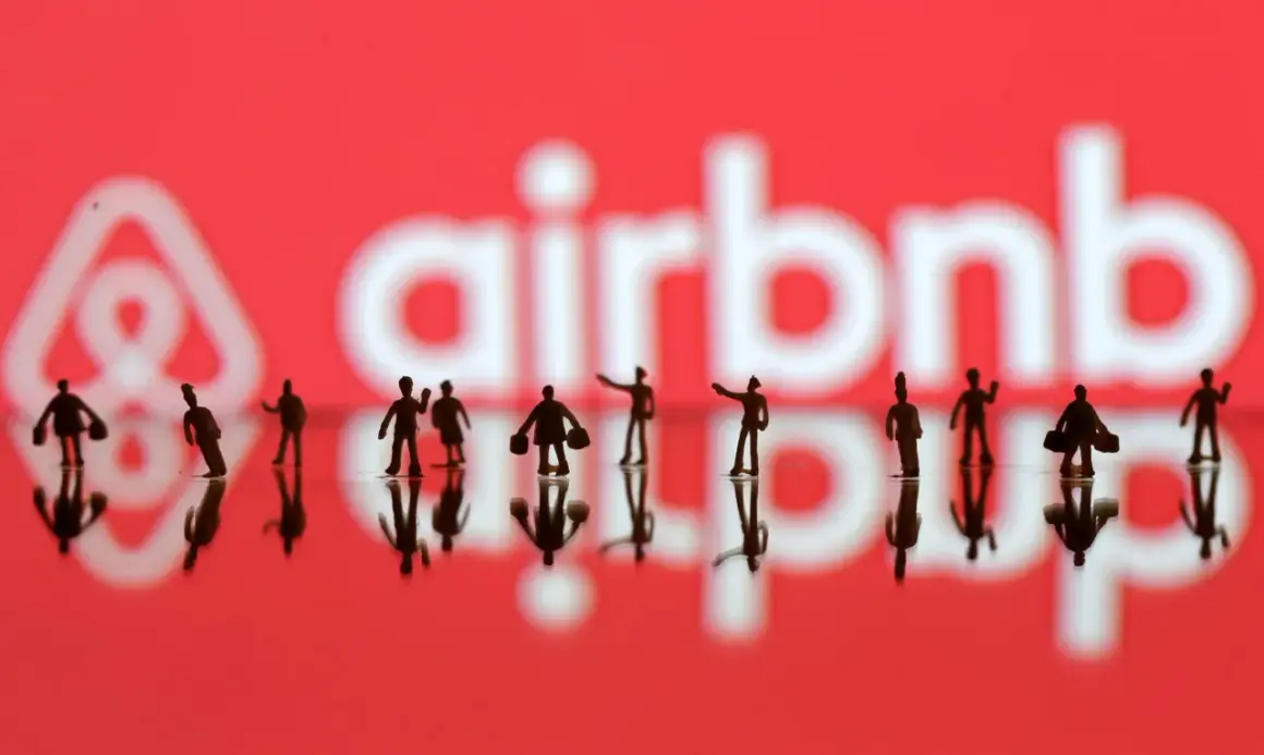 Małe figurki ludzi na tle logo Airbnb. Zastanawiasz się, airbnb co to? To platforma do rezerwacji noclegów i doświadczeń.
