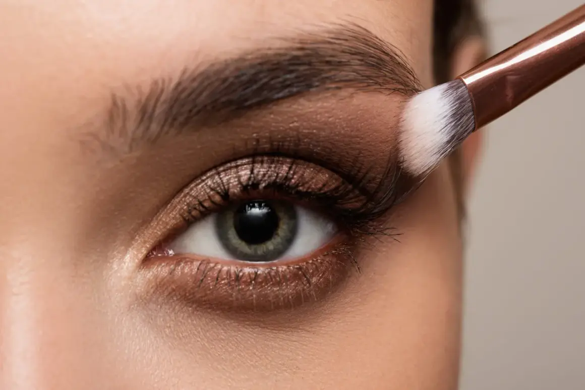 Occhio con trucco elegante, sfumature bronze e un pennello che applica l'ombretto.