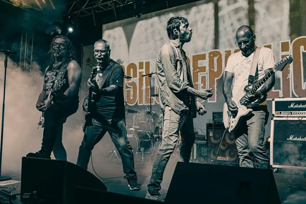 La band "Asilo Republic" sul palco, con chitarristi e cantante in azione, avvolti dal fumo.