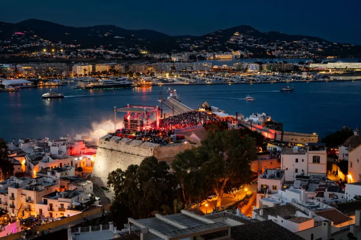 Concerto sul bastione di Dalt Vila, Ibiza, con la baia illuminata e le luci della città. Un evento indimenticabile per chi ama la musica e la magia di IMS Ibiza.