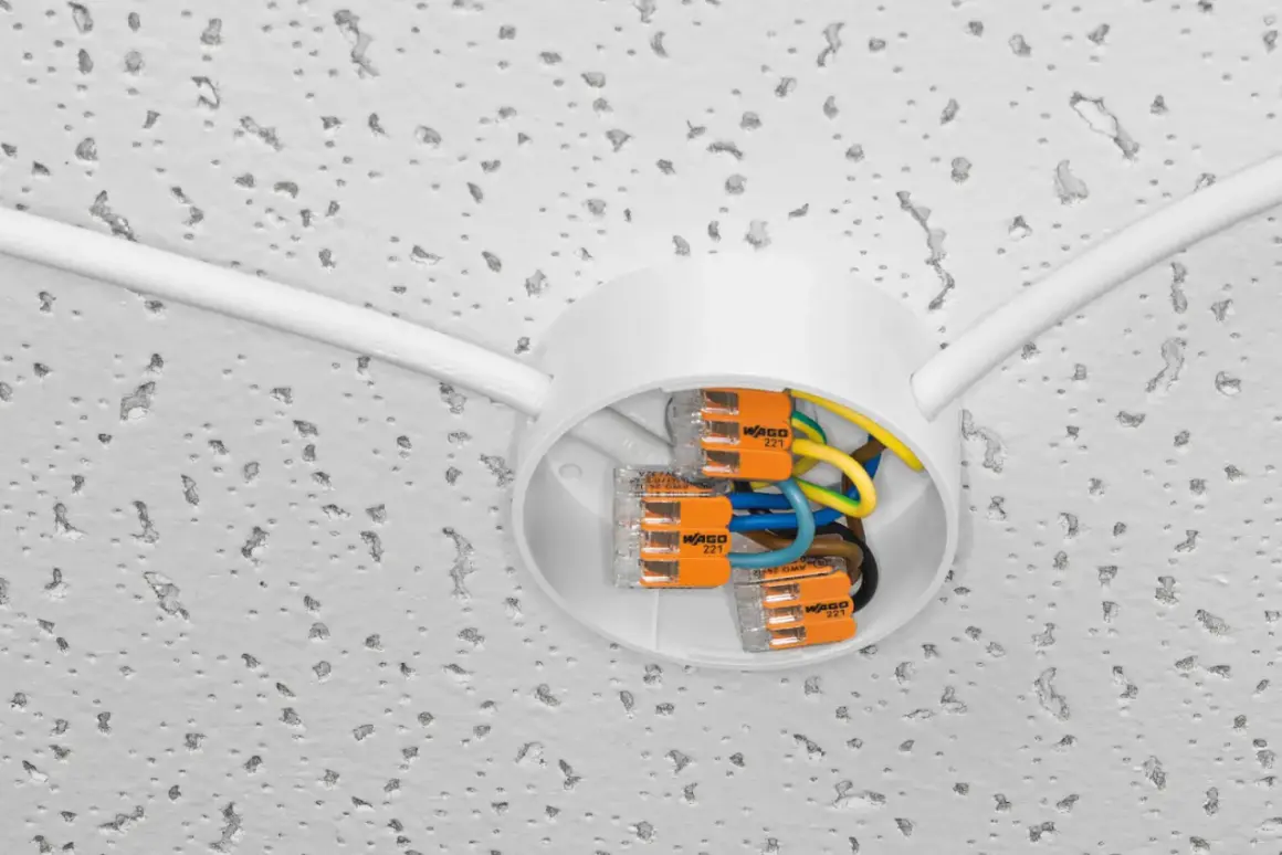 Nowe złącza WAGO ułatwiają wymianę instalacji elektrycznej. Biała puszka sufitowa z kolorowymi przewodami i pomarańczowymi zaciskami.