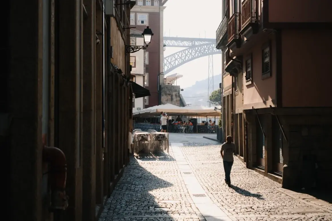 A lone figure walks down a sun-drenched cobblestone street in a European city, a perfect scene for street photography.