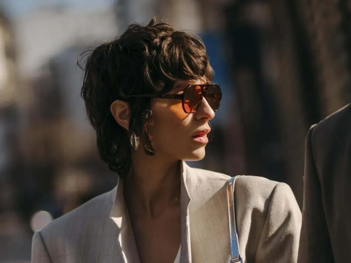 Frau mit einem frechen Pixie Cut, Sonnenbrille und Blazer.