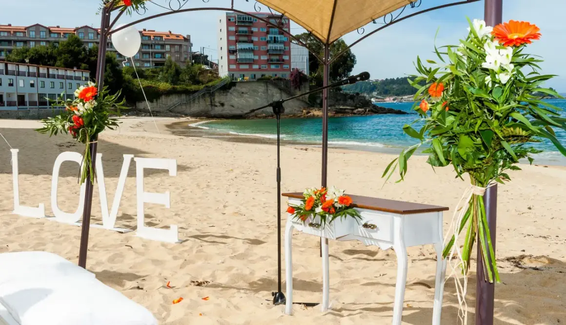 Decoración de boda en la playa de lagos Bueu: letras "LOVE", mesa de altar, flores y el mar azul.