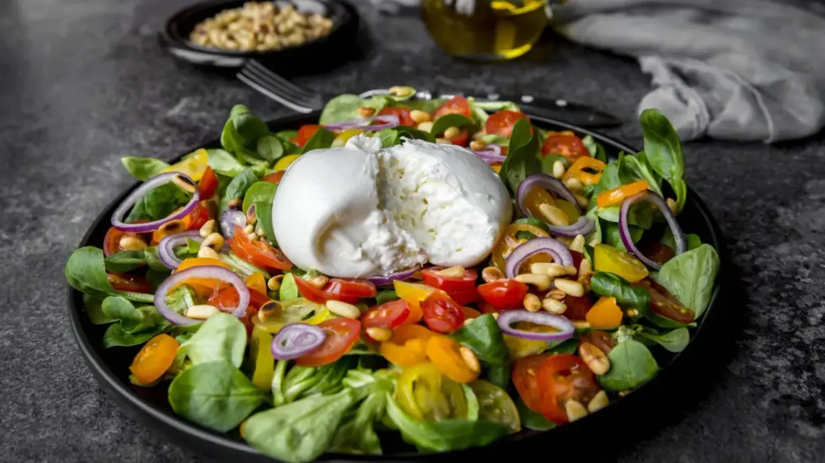 Frischer Salat mit cremiger Burrata, Tomaten, Zwiebeln und Pinienkernen. Perfekt für eine leichte Mahlzeit, auch in der Schwangerschaft.