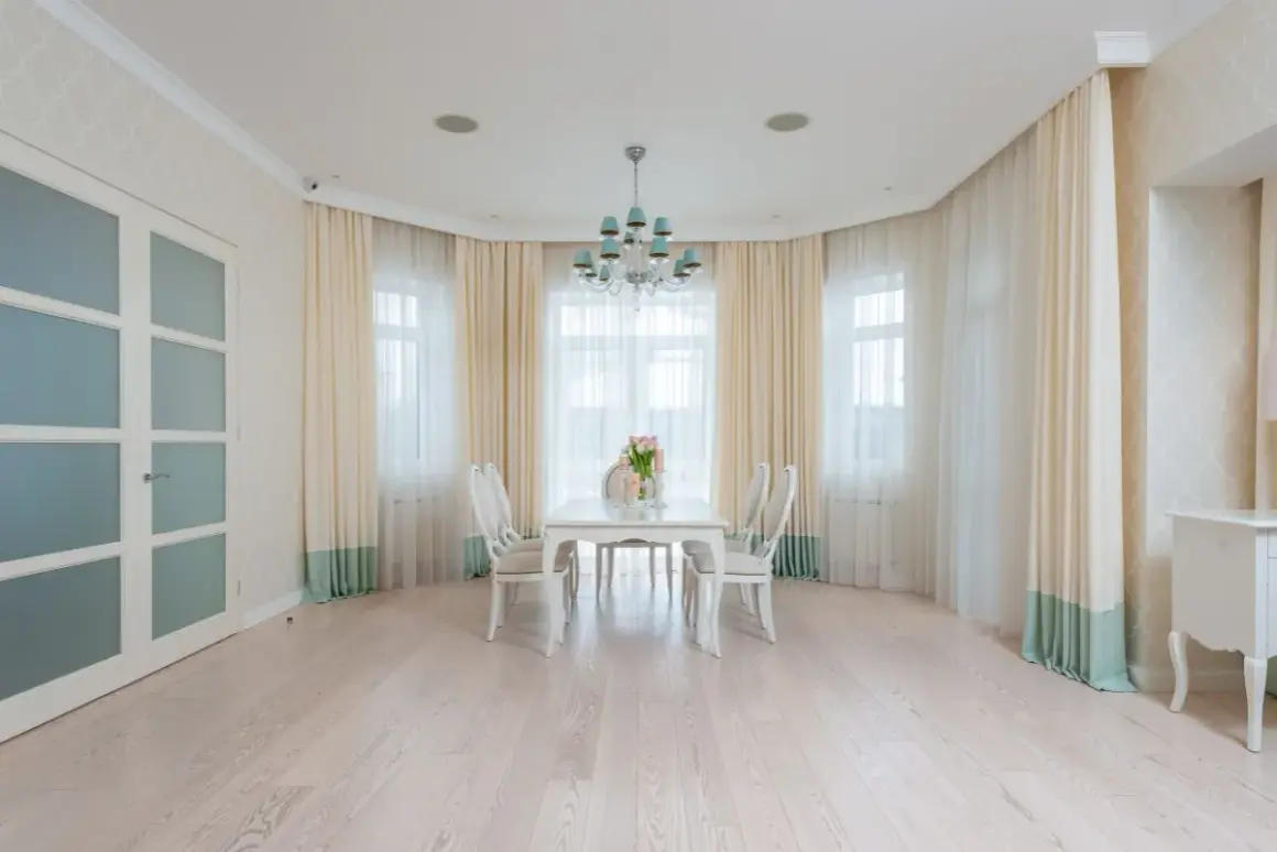 Eleganckie firanki w wykuszu dodają uroku wnętrzu. Jasne zasłony pięknie komponują się z białymi meblami i jasną podłogą.
