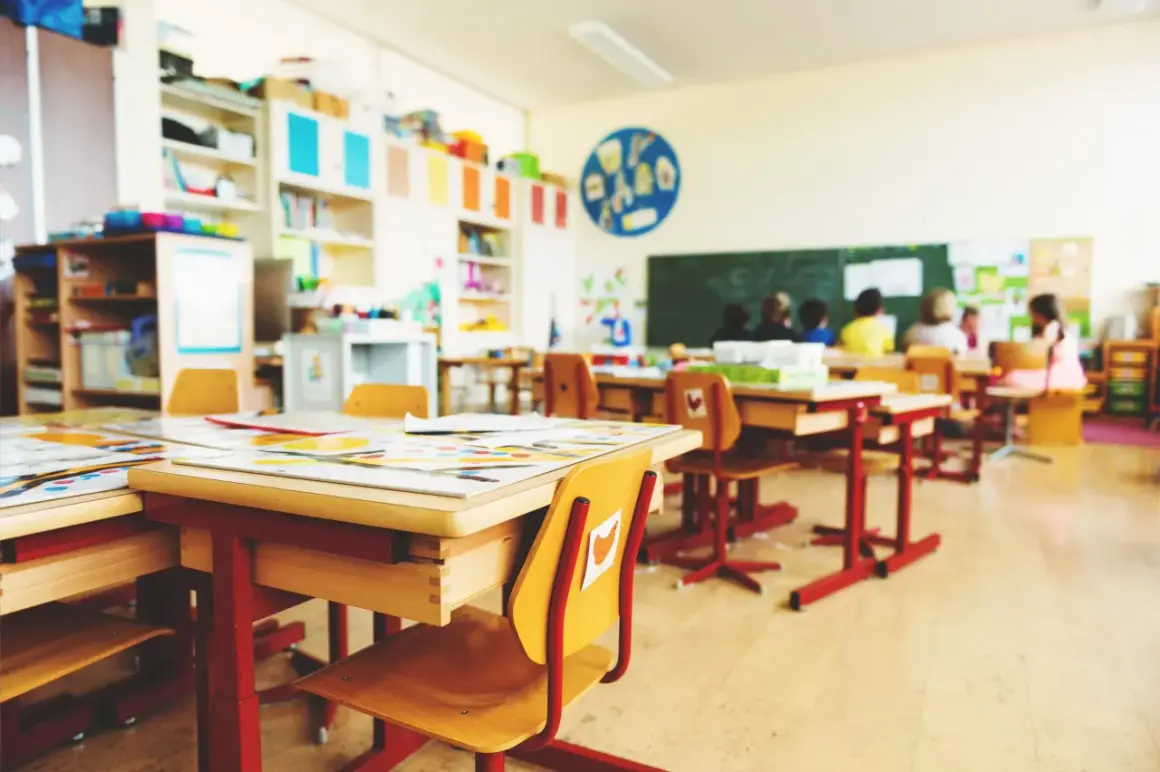 Einladende Raumgestaltung im Klassenzimmer: Helle Tische, bunte Bücherregale und Kinder, die lernen.