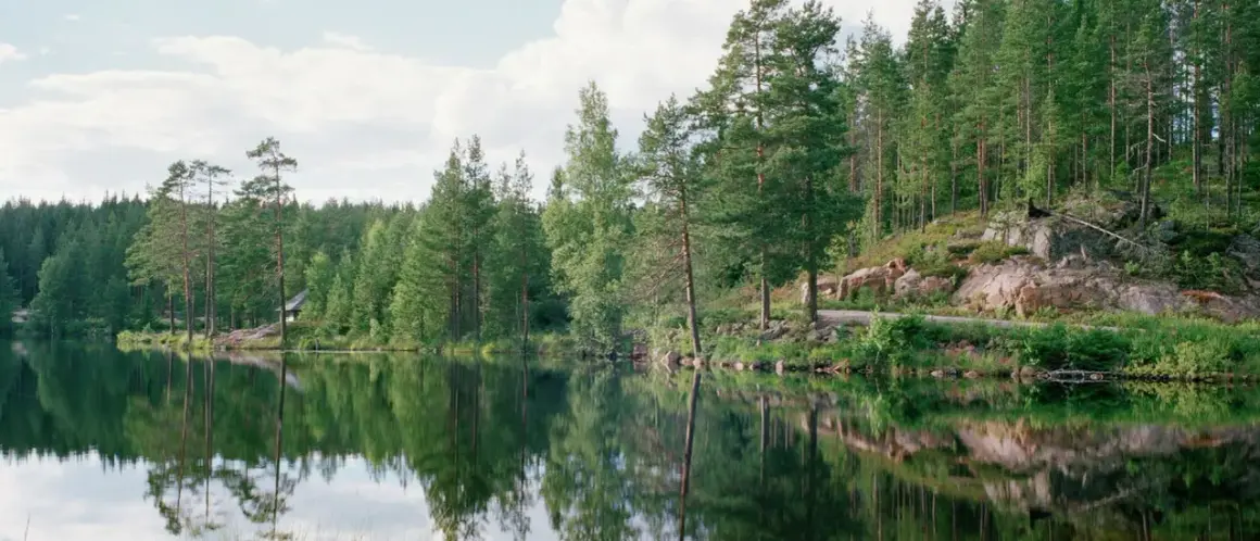 Spegelblank sjö med skog och en liten stuga vid stranden, kanske en del av Malingsbo herrgård.