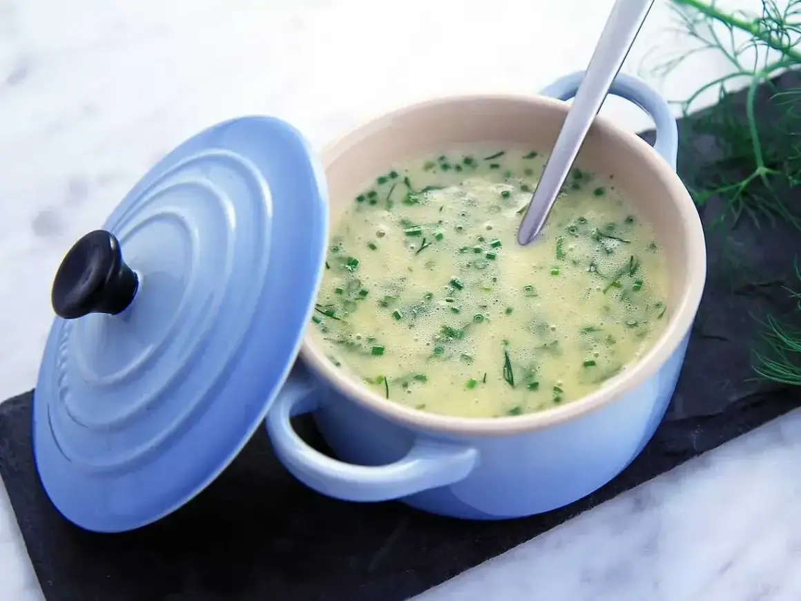 Krämig soppa med dill och gräslök, serverad i en ljusblå gryta. En sked vilar i den lena beurre blanc-såsen.