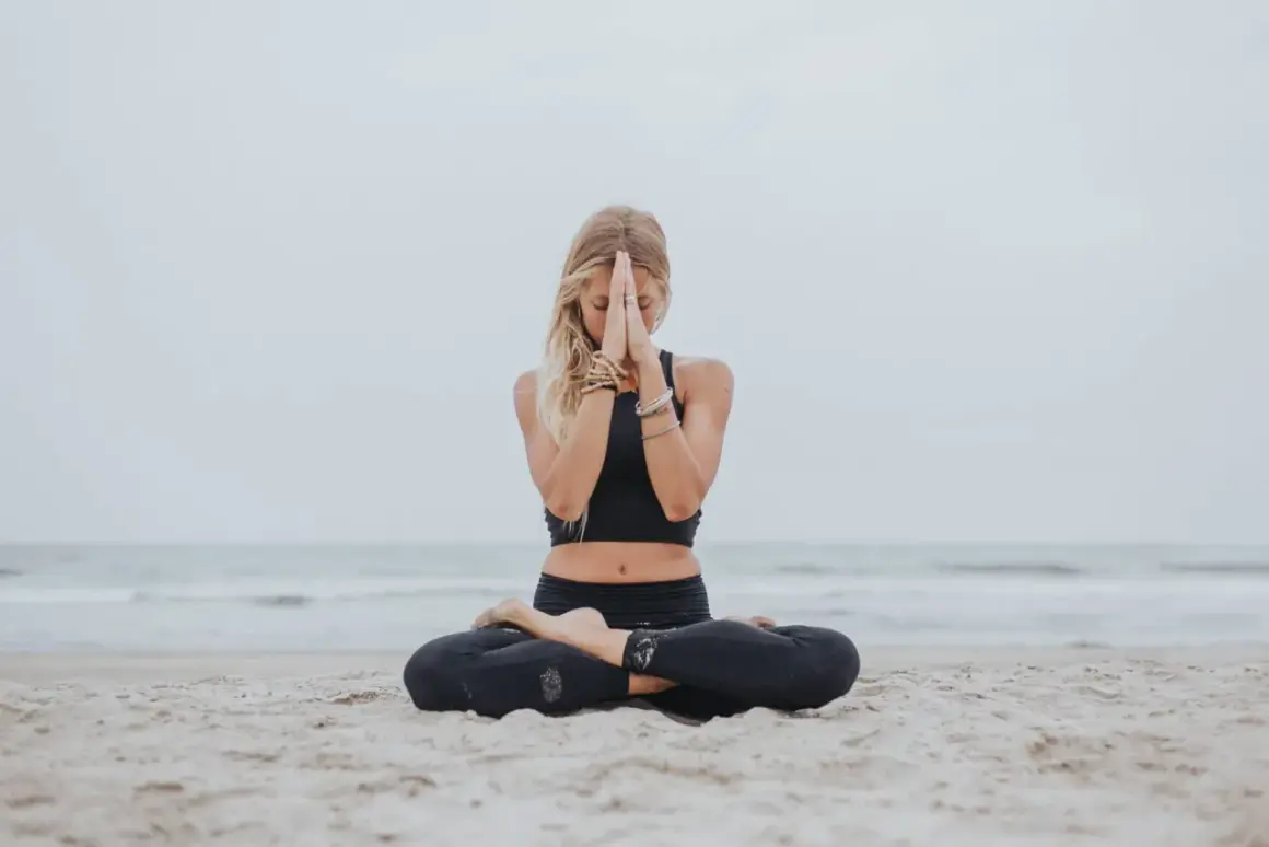 Mujer rubia meditando en la playa, con el gesto namaste. Paz y serenidad en el mar.
