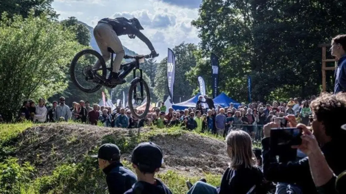 Mountainbiker springt bei einer Veranstaltung in Heubach heute über eine Schanze, während eine Menge zuschaut.