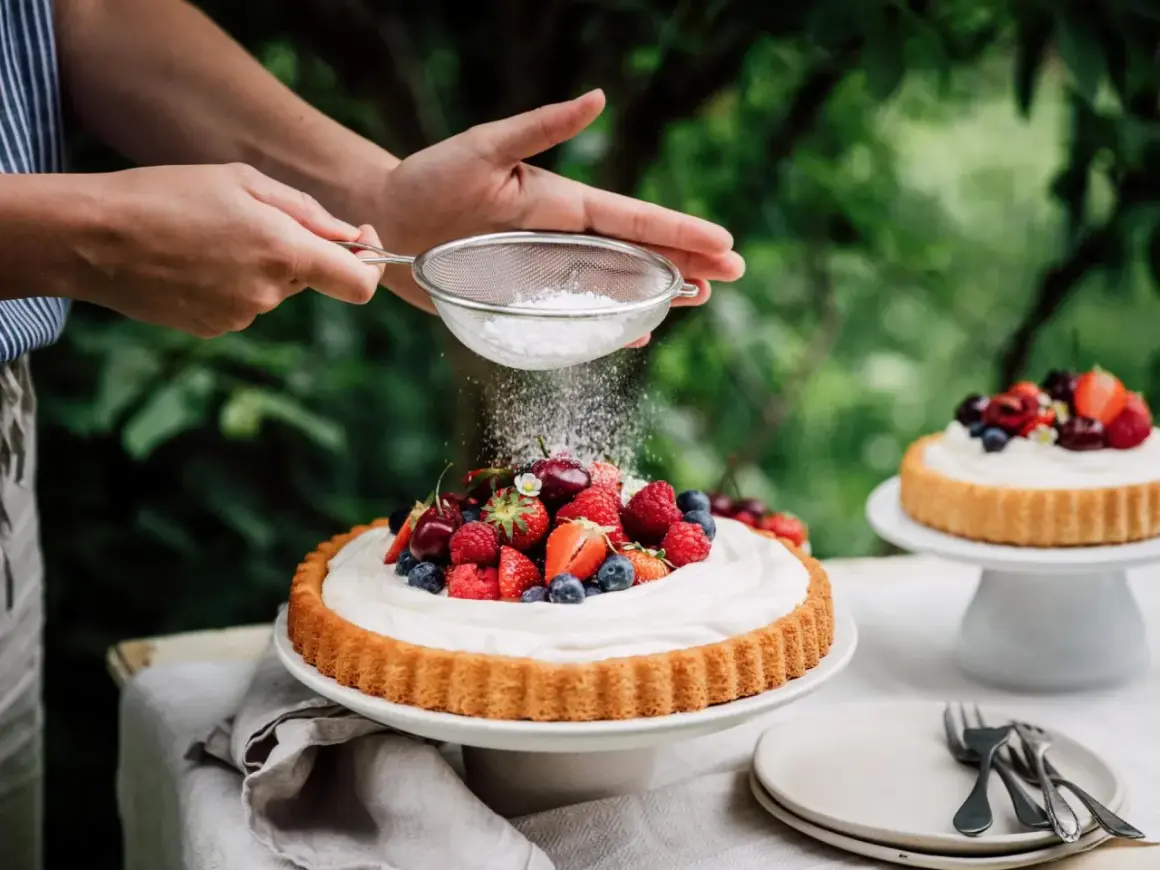 Ein sommerlicher Kuchen mit frischen Beeren wird mit Puderzucker bestäubt.