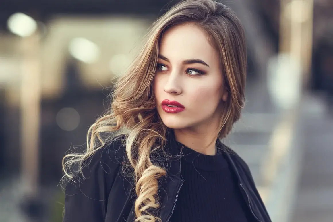 Blondynka z burzą falowanych włosów i wyrazistymi, czerwonymi ustami. Idealny kolor pomadki dla blondynek, który podkreśla urodę.