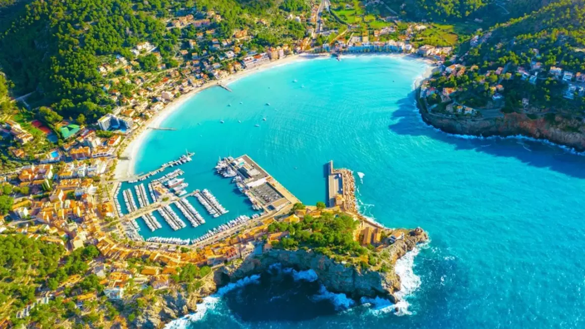 Vacker vy över en turkos bukt med en hamn full av båtar och en stad som klättrar uppför kullarna. En drömsemester i Palma de Mallorca.