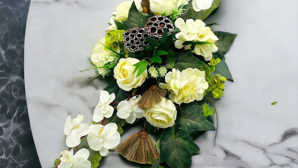 Eleganckie kompozycje funeralne z białych róż, storczyków i ozdobnych łusek lotosu na marmurowym tle.