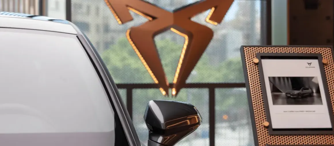 Biały samochód i logo producenta Cupra. Obok zdjęcie nowego modelu Cupra Leon PHEV.