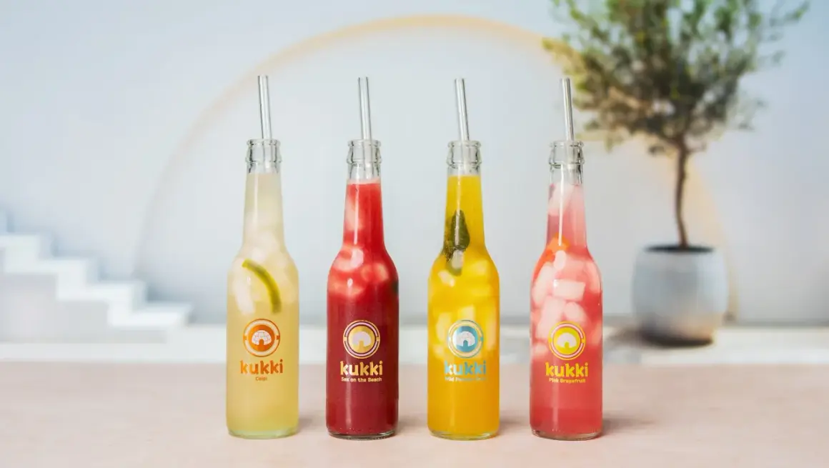 Vier bunte Kukki Cocktails mit Eis und Strohhalmen, bereit zum Auftauen und Genießen.