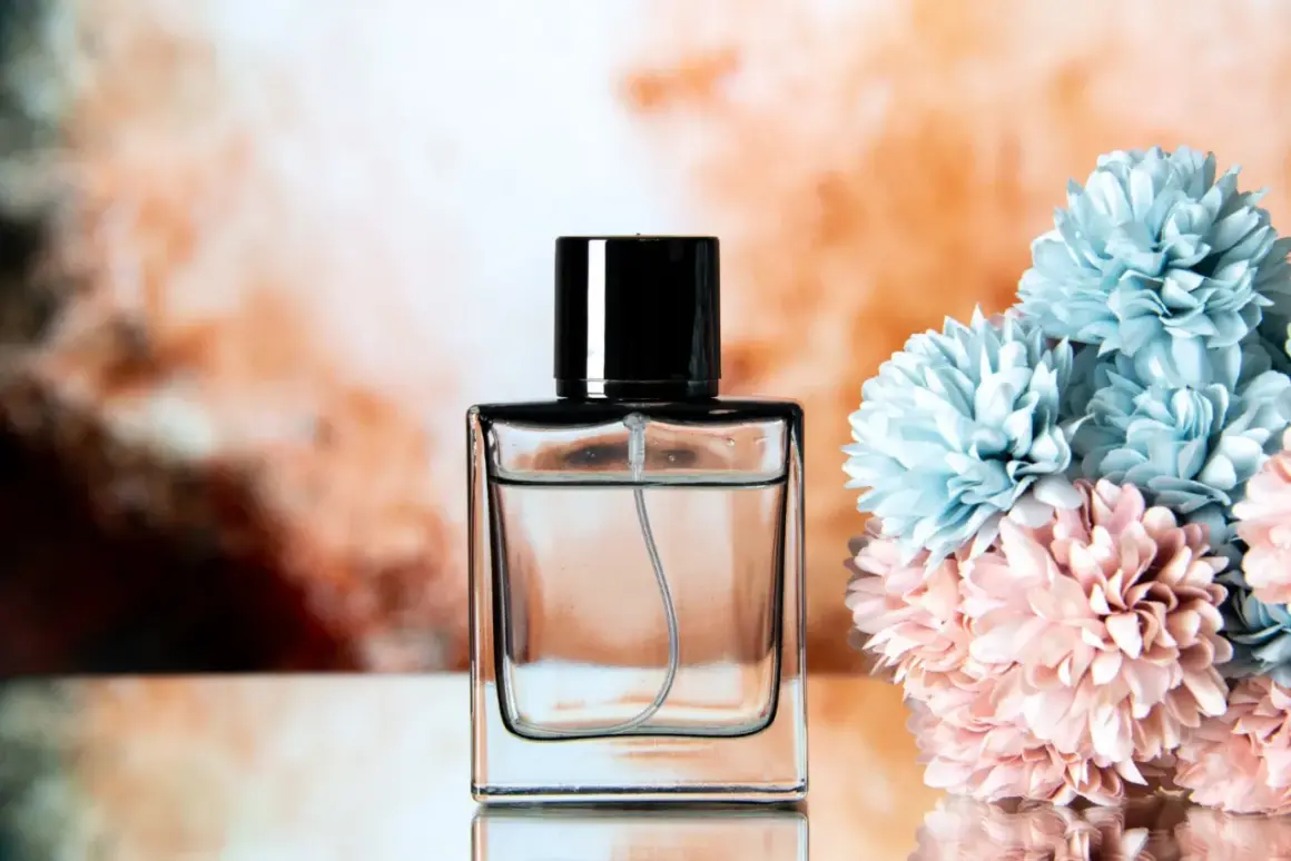 Elegancka butelka perfum z czarną nakrętką, obok bukiet pastelowych kwiatów. Chcesz wiedzieć, jak sprawdzić oryginalność perfum?