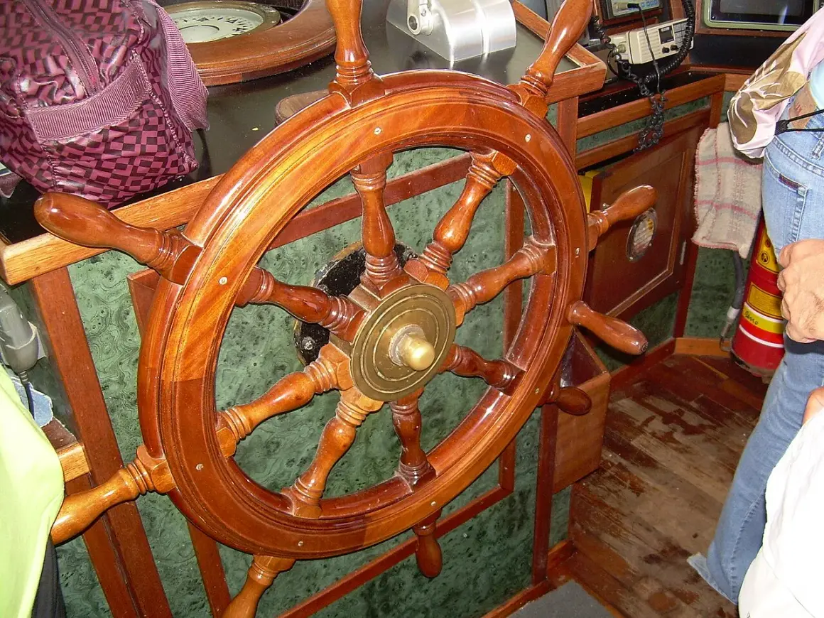 Il timone, come si chiama il volante della nave, è di legno lucido, pronto a guidare.