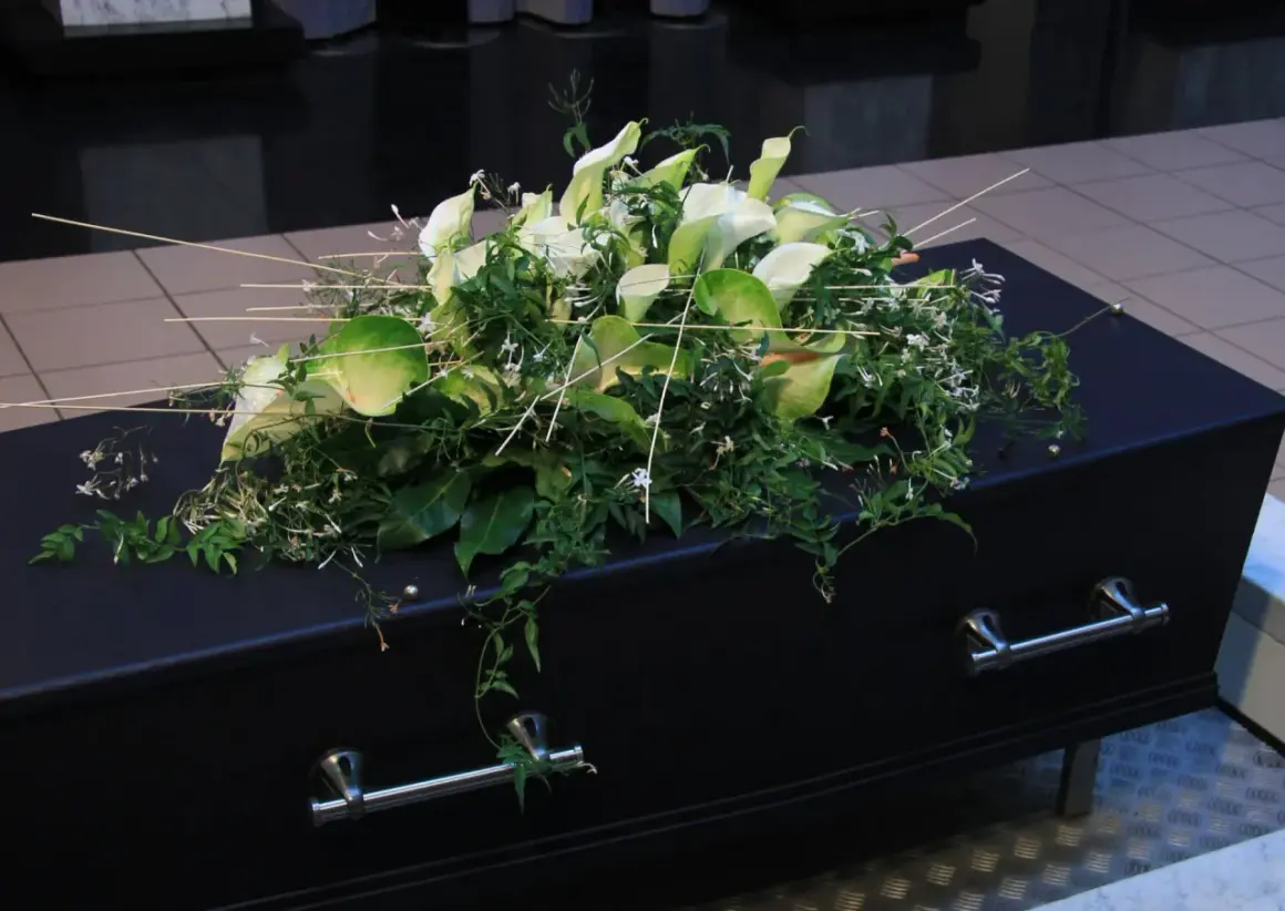 Elegancki wieniec z białych kalii i zieleni spoczywa na czarnej trumnie. To ostatnie pożegnanie, wieniec dla taty.