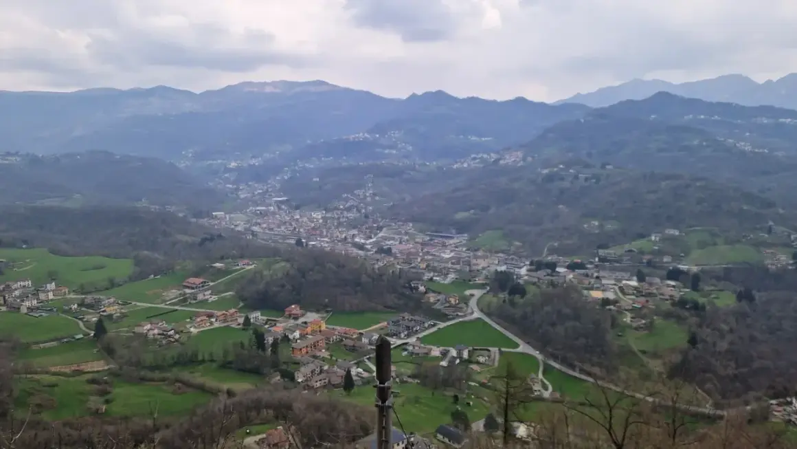 Panoramica della valle Imagna con case sparse tra colline verdi e montagne nebbiose sullo sfondo.