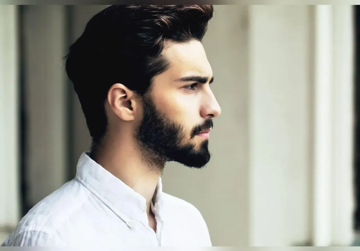 Profil d'un homme avec une barbe haute sur les joues, portant une chemise blanche.