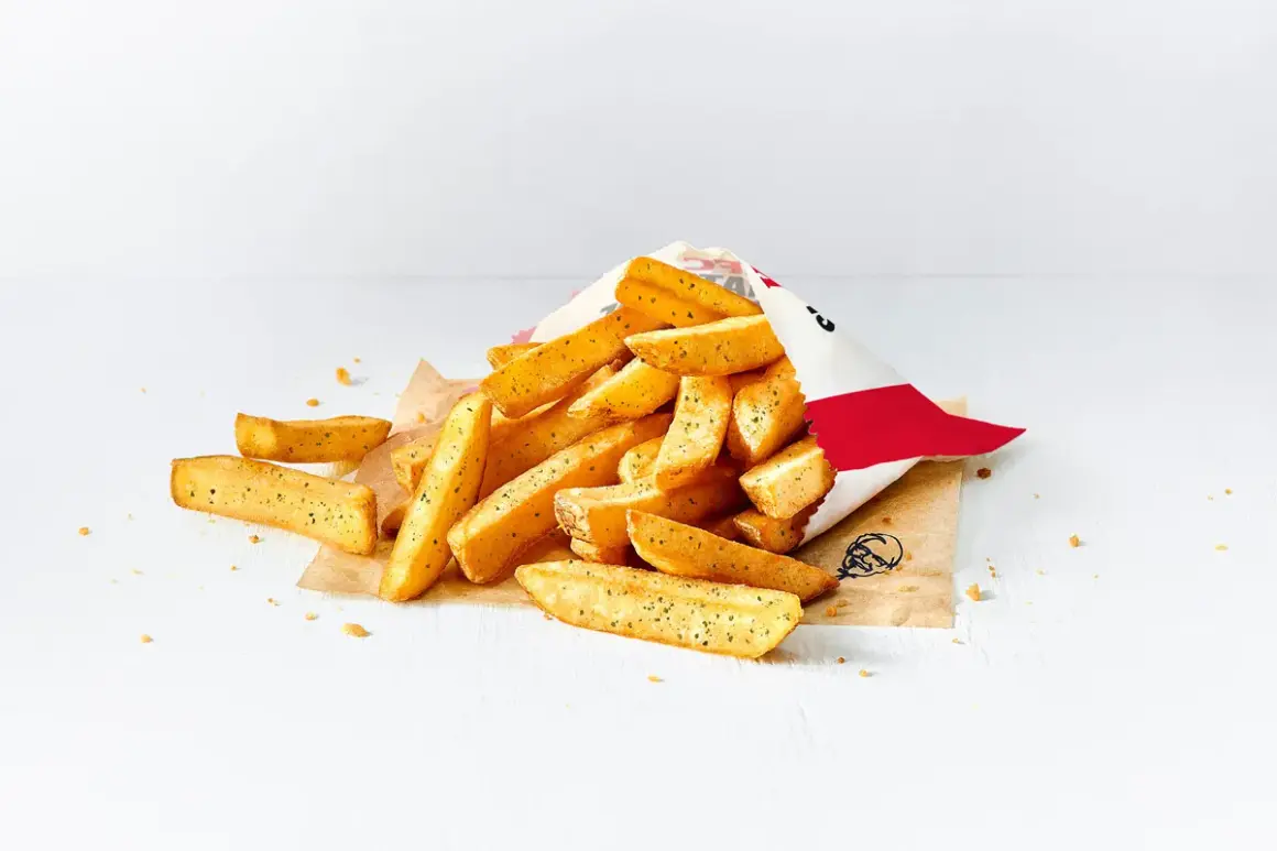 Stos małych frytek z KFC wysypany z papierowej torebki na białym tle.