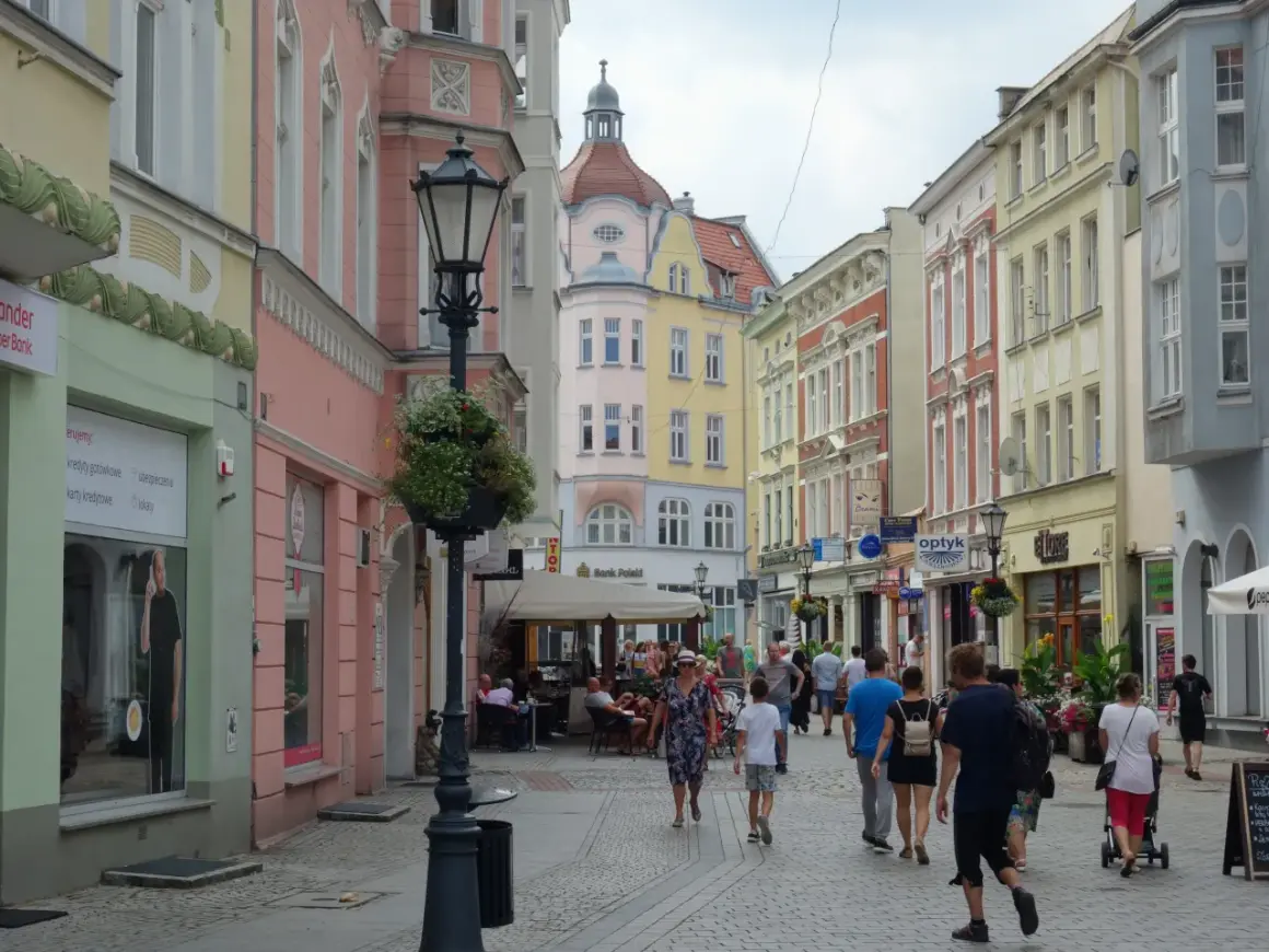 Kolorowa ulica z kamienicami, latarnią i ludźmi spacerującymi po deptaku. Zielona Góra oferuje wiele atrakcji.